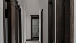 A narrow hallway with wooden doors on both sides and a visible door at the end leading to a room. - Polar Den Cabin - Pet Friendly! (Valemount)