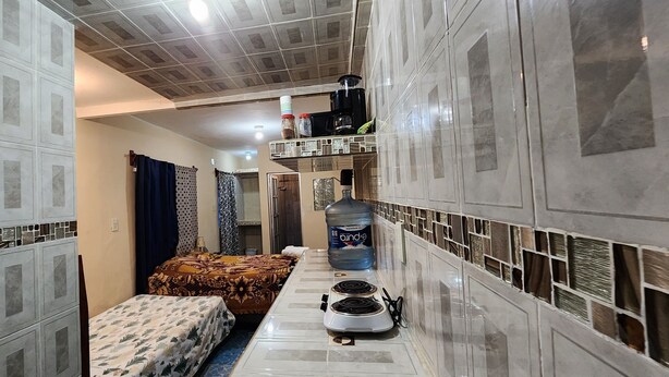 A narrow hotel room with a kitchenette, a bed with a floral bedspread, and a blue curtain.