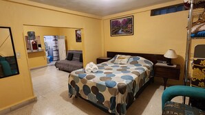 Ein Hotelzimmer mit Bett, Nachttisch, Lampe, Stuhl, Etagenbett, Badezimmer und einem Bild an der Wand.