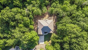 An aerial view of a house surrounded by dense forest. - 5BR Bentonville Area Retreat | Sleeps 14 | 3 King Beds | GameRoom & Deck Firepit (Bella Vista)