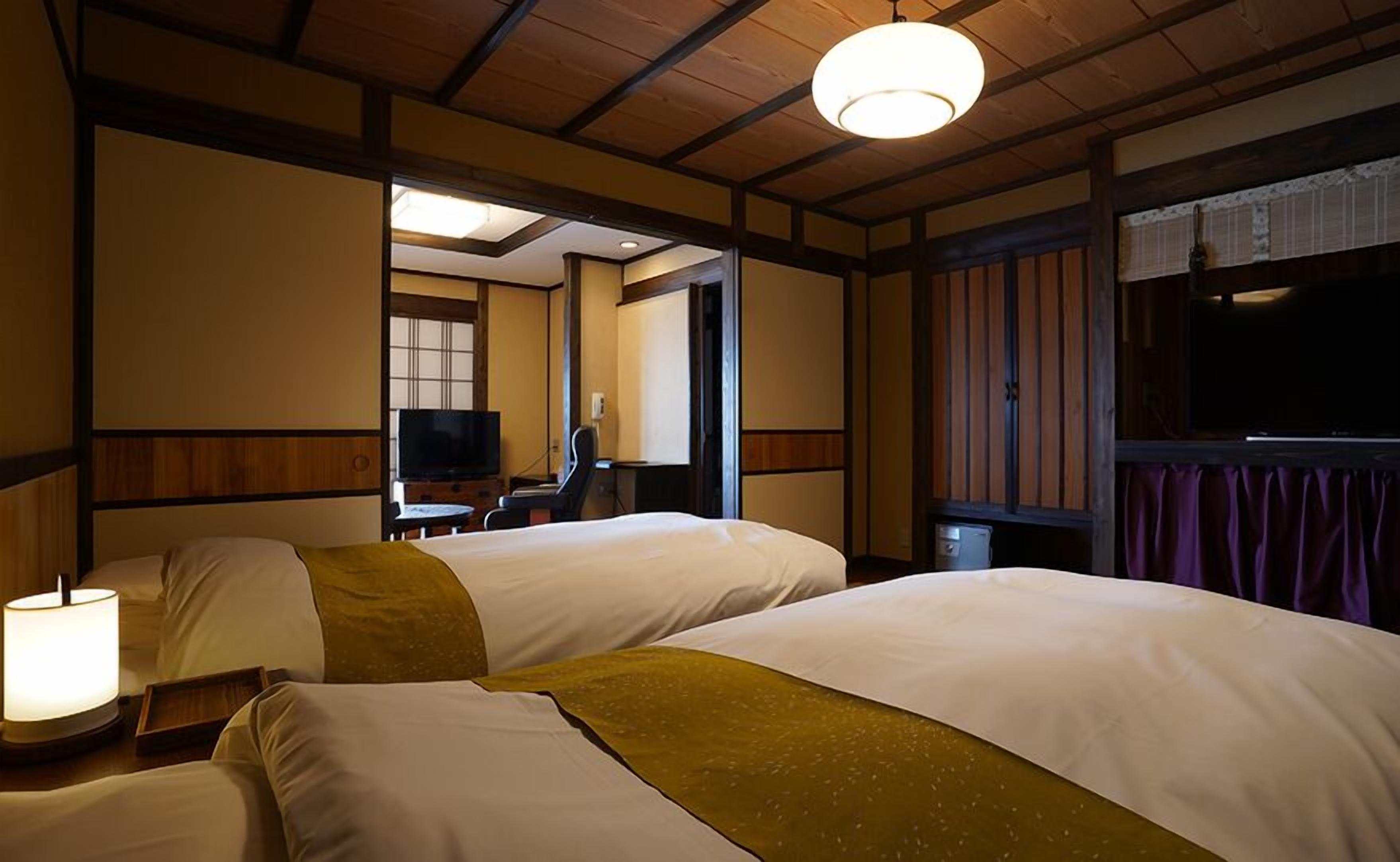 A hotel room with two beds, a television, a desk, and a window with curtains.