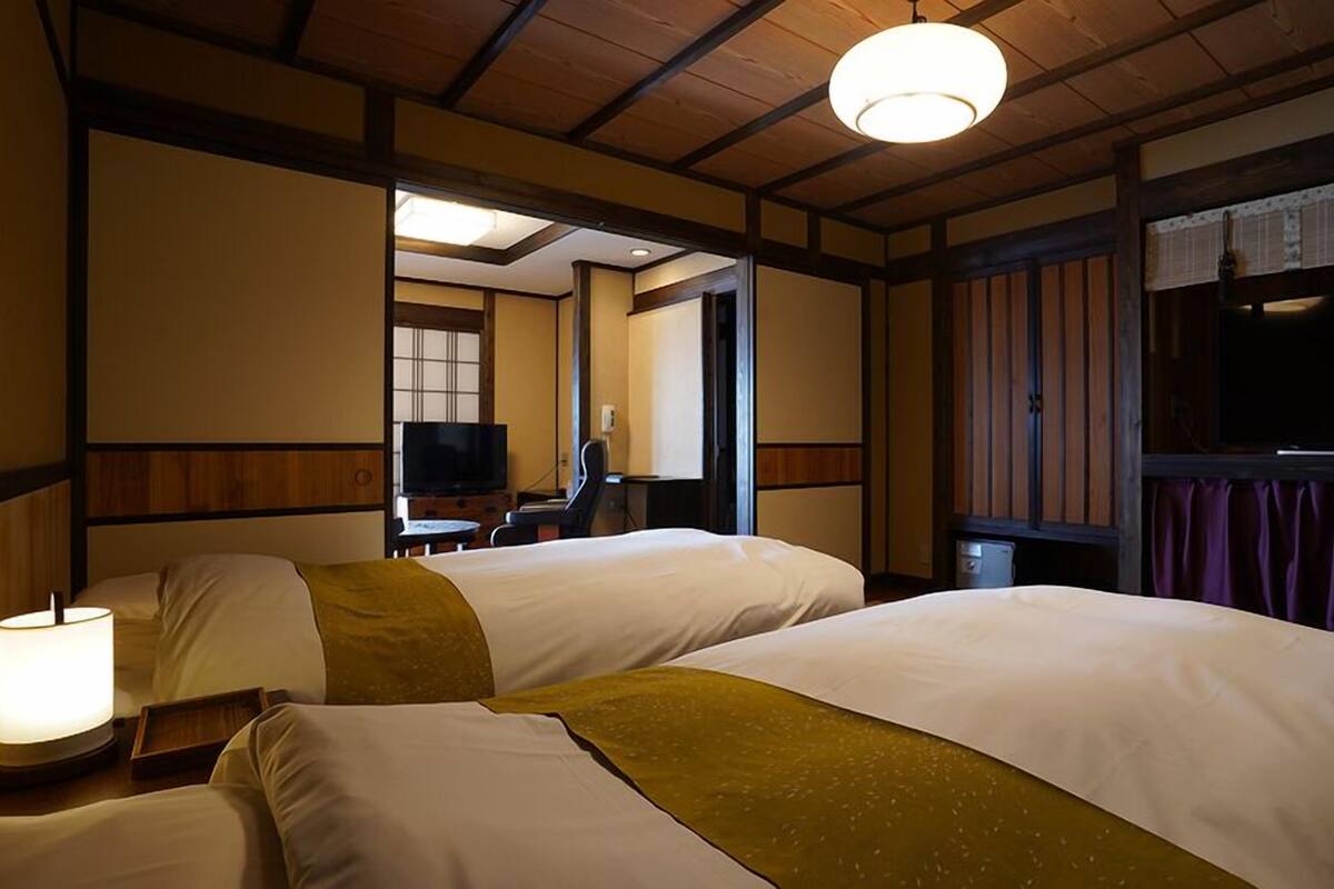 A hotel room with two beds, a television, a desk, and a window with curtains.