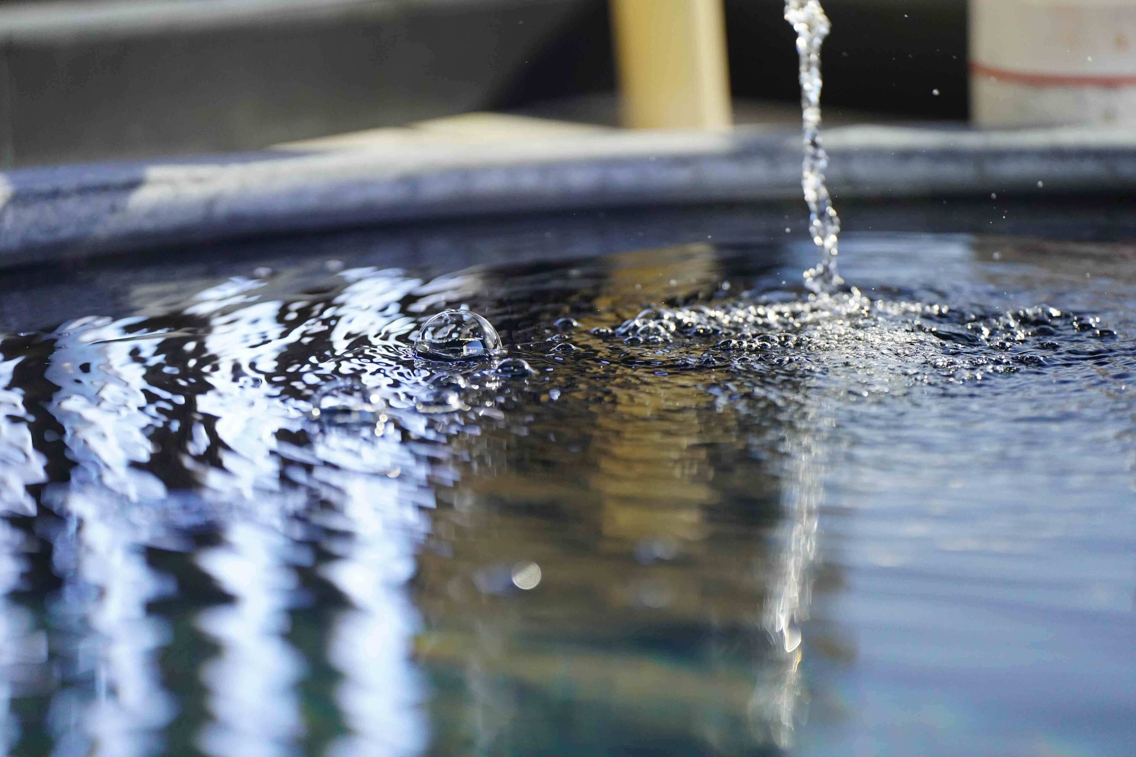 A close-up of water splashing into a pool, creating ripples and bubbles.