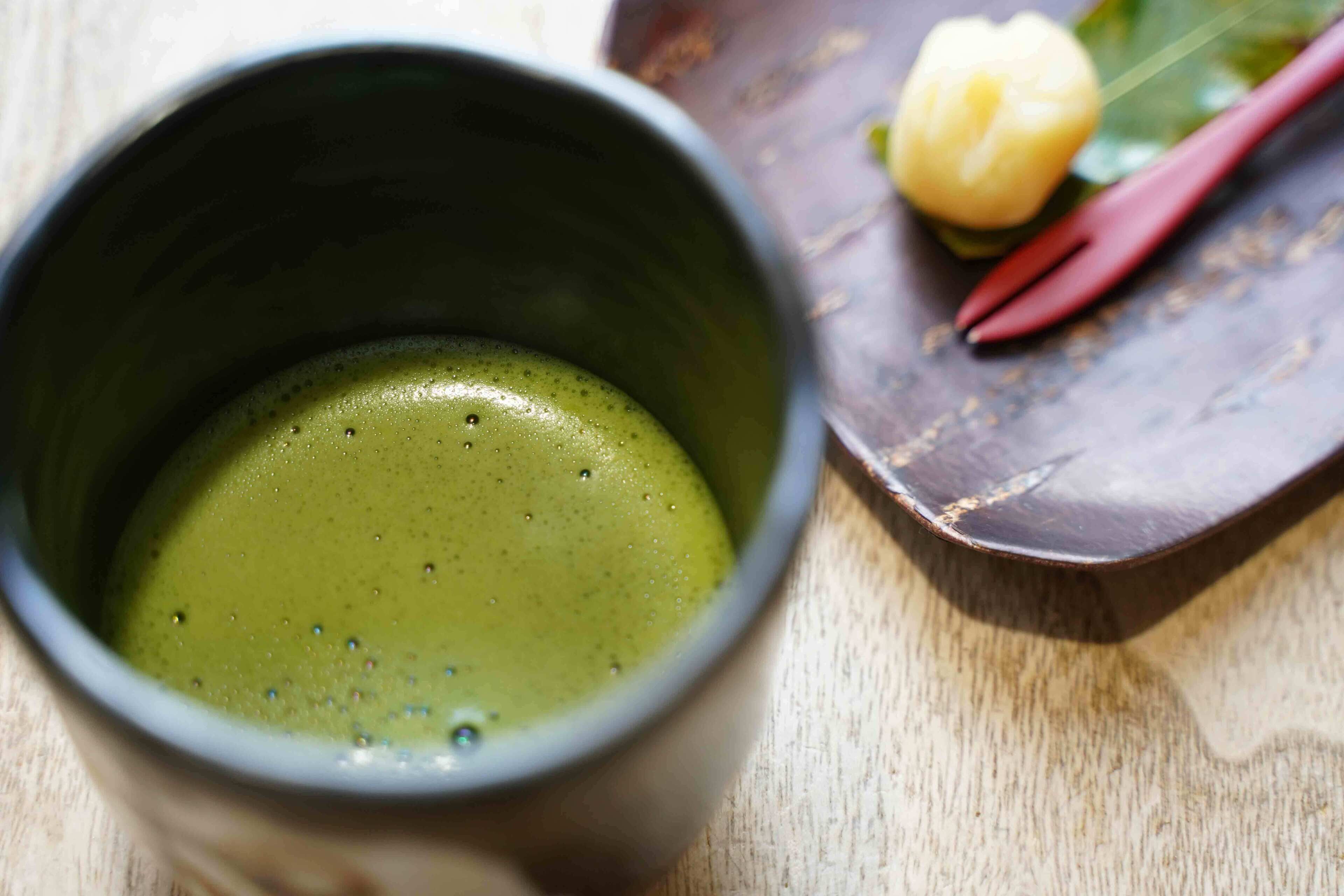 A cup of green tea with a wooden table and a decorative item in the background.