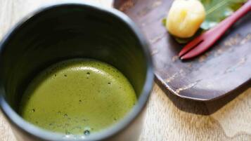 A cup of green tea with a wooden table and a decorative item in the background.