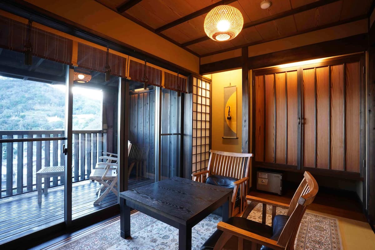 Una habitación japonesa tradicional con suelo de tatami, puertas correderas, una mesa de madera y vistas a un área boscosa.