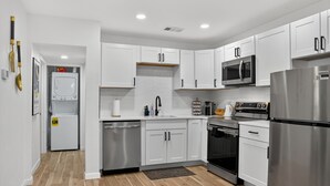 A modern kitchen with white cabinets, stainless steel appliances, and a wooden floor.