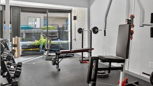 A gym with weightlifting equipment, a bench, and a view of a balcony with outdoor seating.