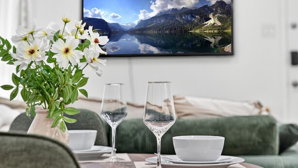 A dining table with a vase of white flowers, two wine glasses, and a bowl on a placemat.