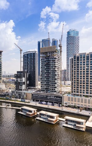 A modern urban waterfront with high-rise buildings, including a construction site and a canal with boats.