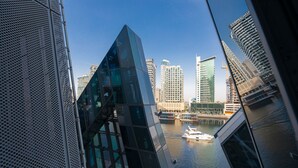 A modern building with a glass facade and a view of a river with a boat. - LUX Waterfront 1BR near B Khalifa (Dubai)