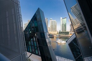 A modern building with a glass facade and a view of a river with a boat. - LUX Waterfront 1BR near B Khalifa (Dubai)