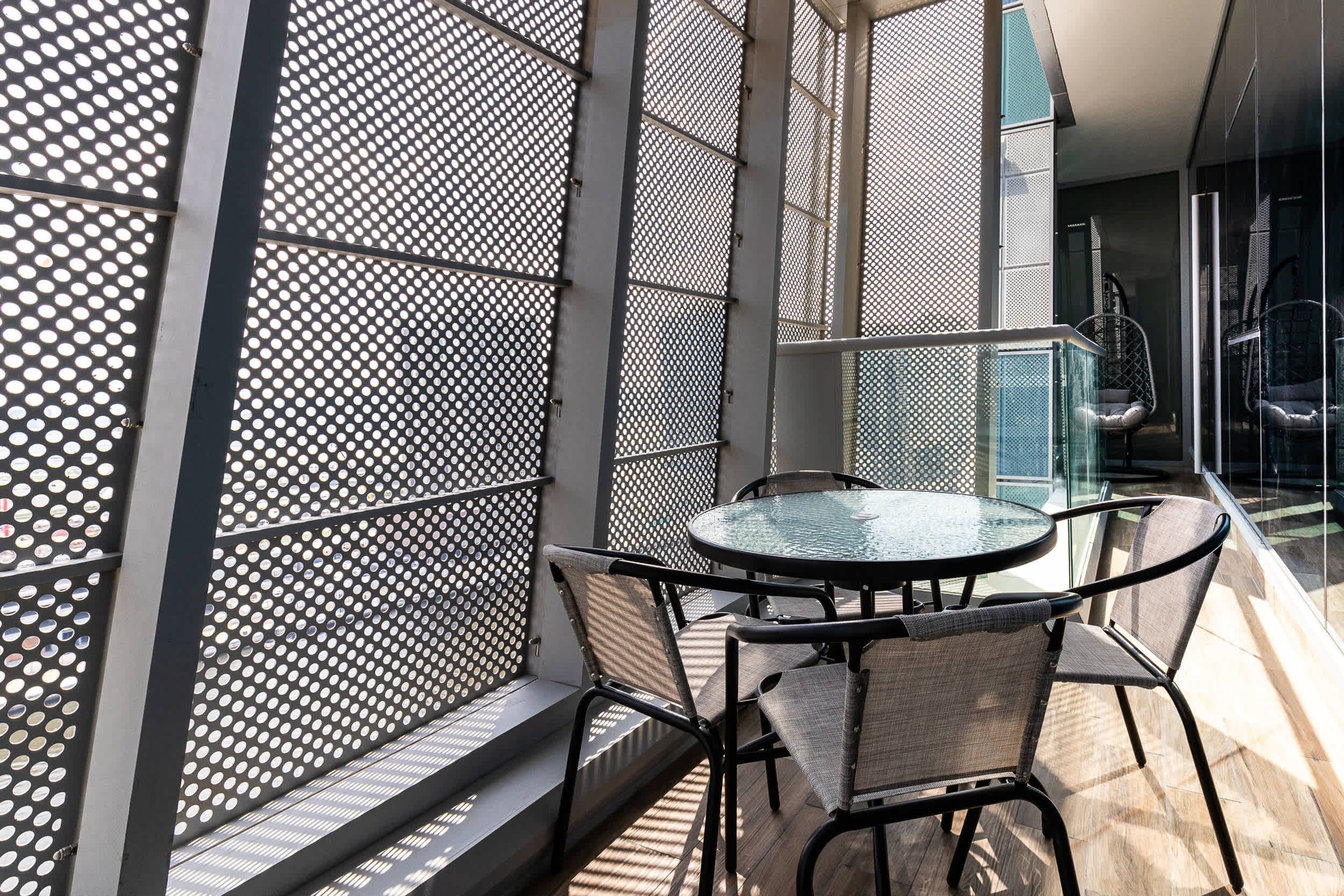 A balcony with a glass table and chairs, a metal fence, and a view of the interior.