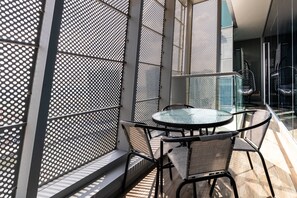A balcony with a glass table and chairs, a metal fence, and a view of the interior.