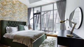 A bedroom with a large bed, a desk with a lamp, a balcony with a table and chairs, and a patterned wallpaper. - LUX Waterfront 1BR near B Khalifa (Dubai)