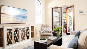 Ein Wohnzimmer mit einem großen Flachbildfernseher, einem beige farbenen Sofa, einem Couchtisch und einer Vitrine.