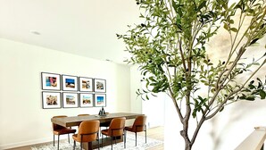 A dining area with a wooden table and chairs, a rug, and framed pictures on the wall. - Modern 3-Story Condo Across from Arnold’s Park – Walk to Fun, Lake, & Dining! (Arnolds Park)