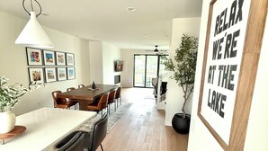 A modern kitchen with a dining area, wooden flooring, and a large framed sign on the wall. - Modern 3-Story Condo Across from Arnold’s Park – Walk to Fun, Lake, & Dining! (Arnolds Park)