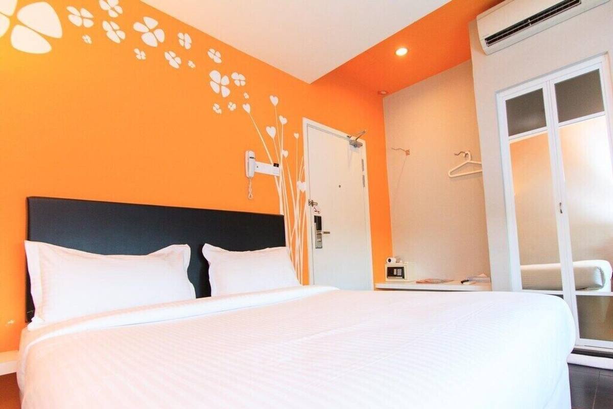 Una habitación de hotel con una cama grande, una pared naranja, una puerta blanca y una ventana con vistas.
