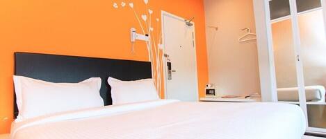 Una habitación de hotel con una cama grande, una pared naranja, una puerta blanca y una ventana con vistas.