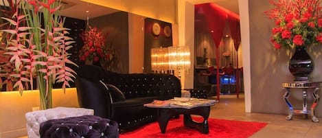 A modern living room with a black sofa, a red rug, and decorative plants.