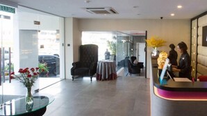 Un hall d’hôtel comprenant un comptoir d’accueil, un espace salon et une grande fenêtre donnant sur les voitures garées.