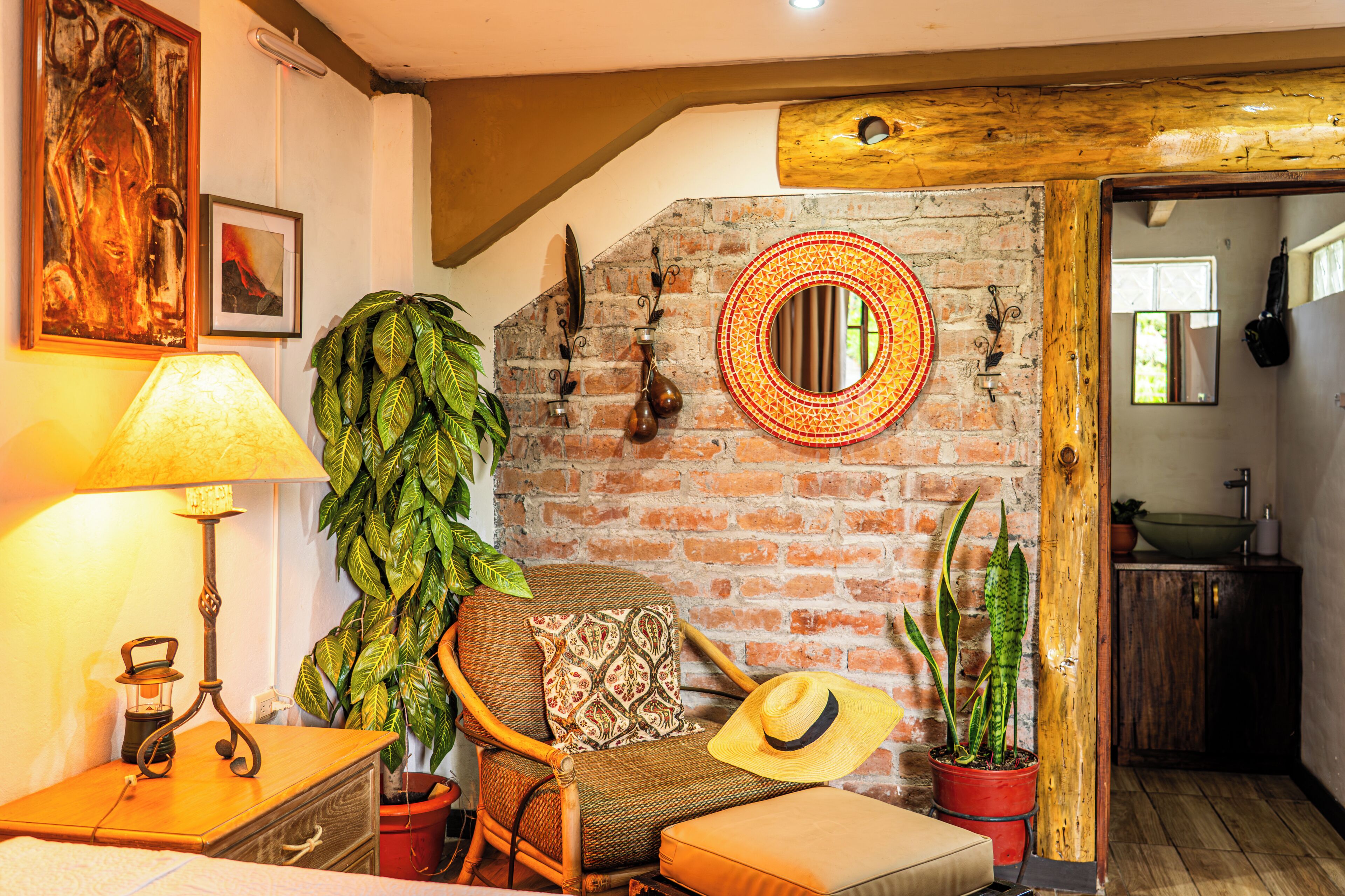 Una habitación acogedora con pared de ladrillo, techo de madera, espejo redondo, sillón mecedor, lámpara y plantas en macetas.