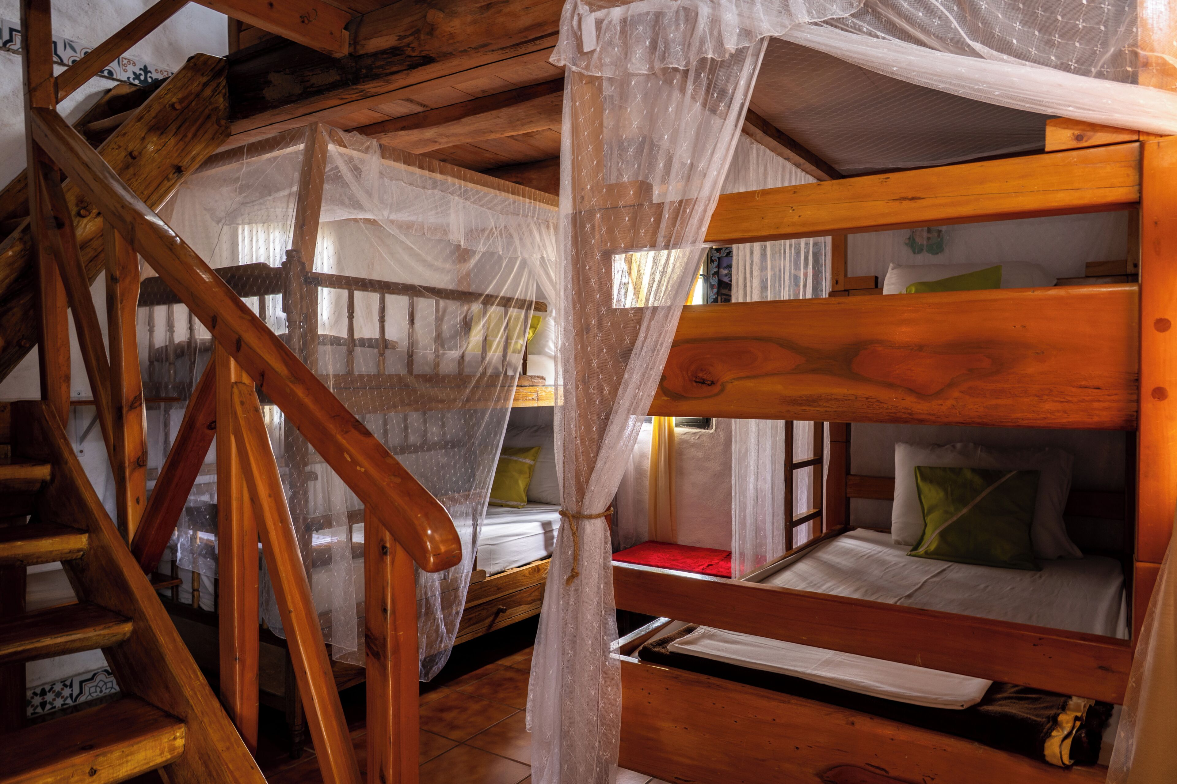 Ein Holzhütten-Interieur mit einem Stockbett, einer Treppe und einem Moskitonetz.