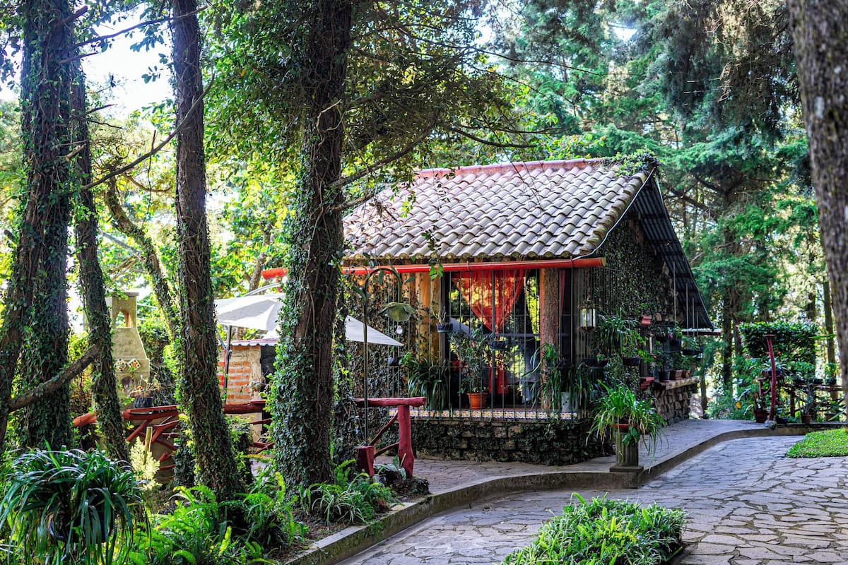 Un bâtiment traditionnel, doté d’un toit en tuiles, entouré d’une végétation luxuriante et de sentiers pavés de pierres.
