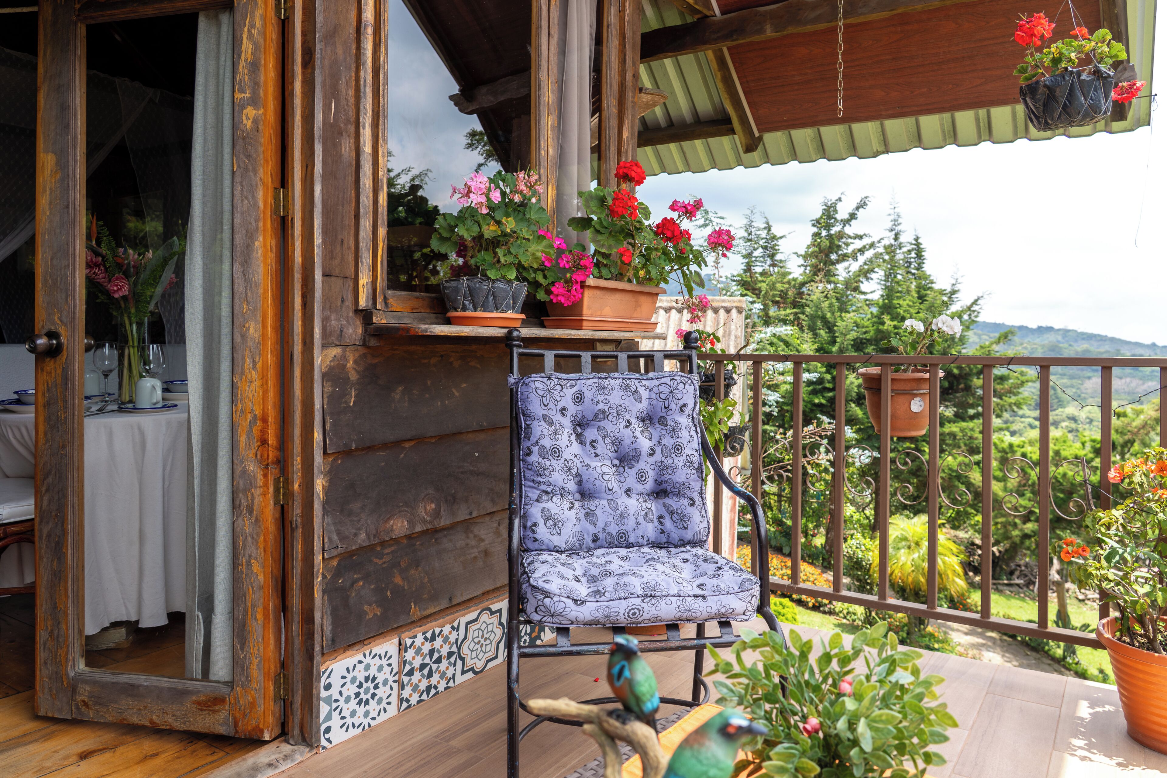 A wooden balcony with a chair, potted plants, and a view of the landscape.