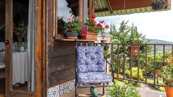 A wooden balcony with a chair, potted plants, and a view of the landscape.