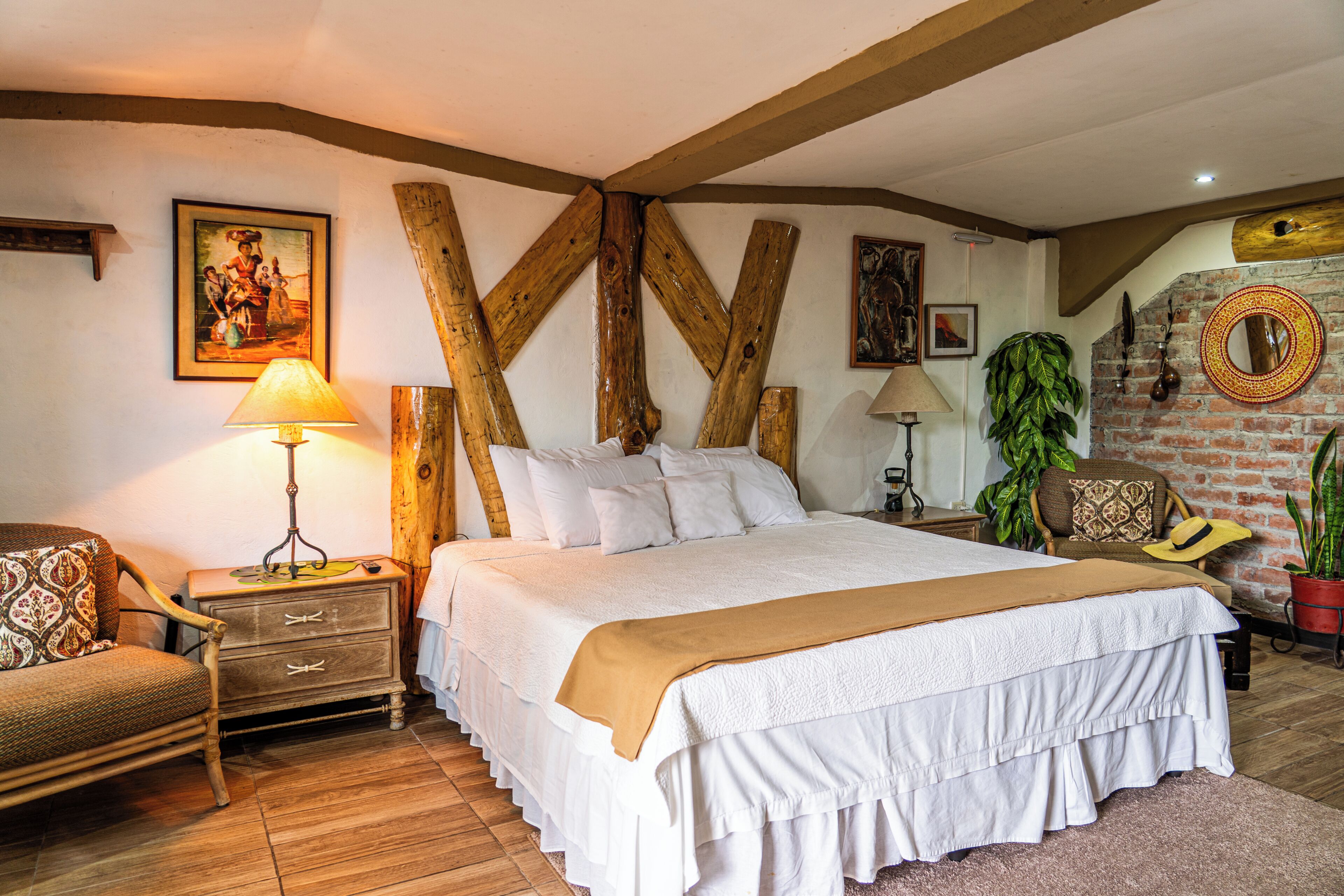 Un dormitorio con una cama grande, vigas de madera, una mesita de noche de madera, una silla, una lámpara y una planta en maceta.