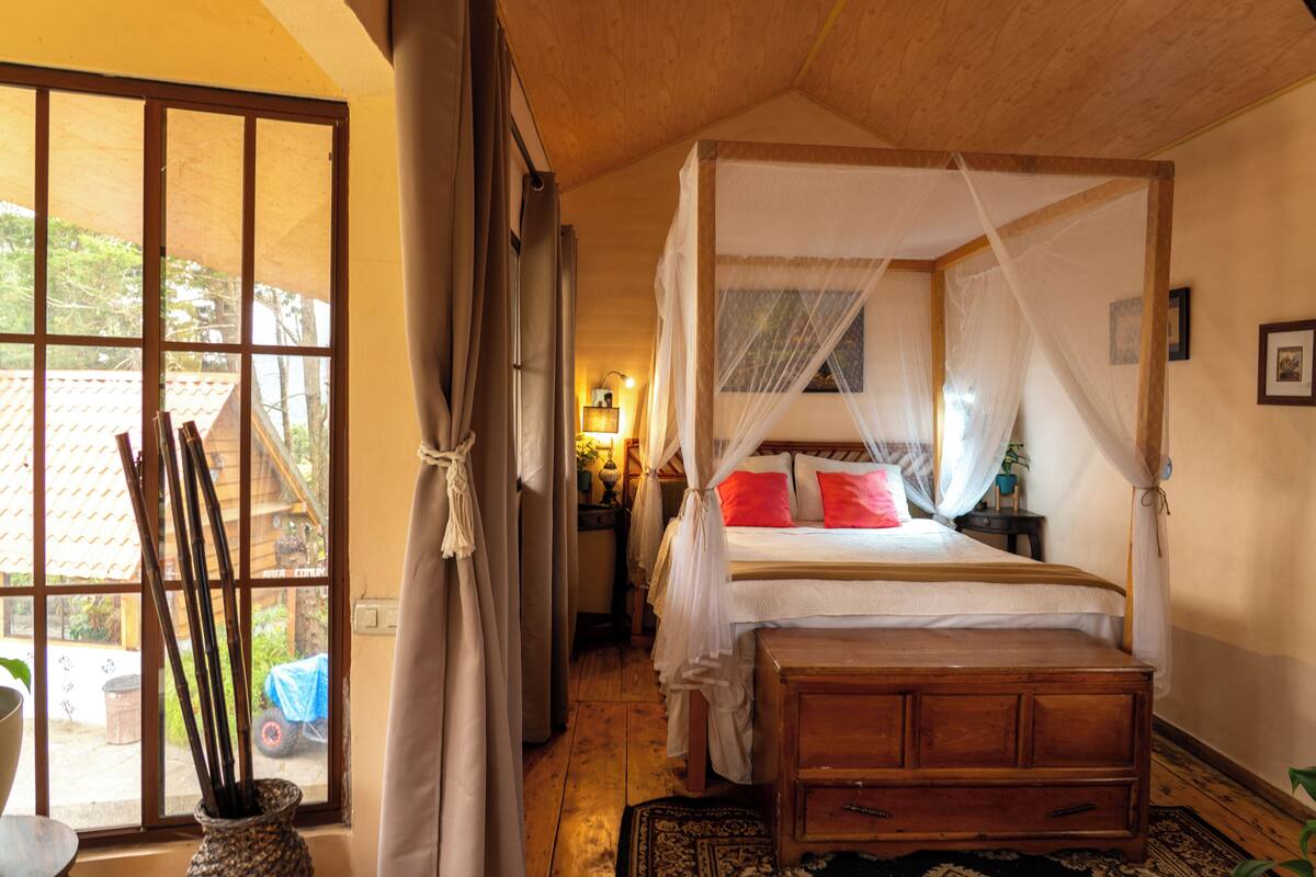 Une chambre à coucher avec un lit en bois, une fenêtre avec des rideaux et une table de chevet avec une lampe.