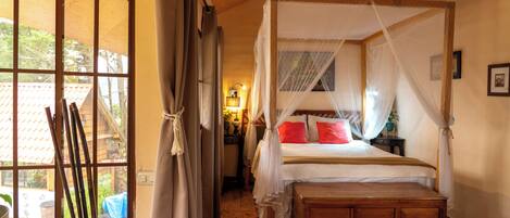 A bedroom with a wooden bed, a window with curtains, and a nightstand with a lamp.