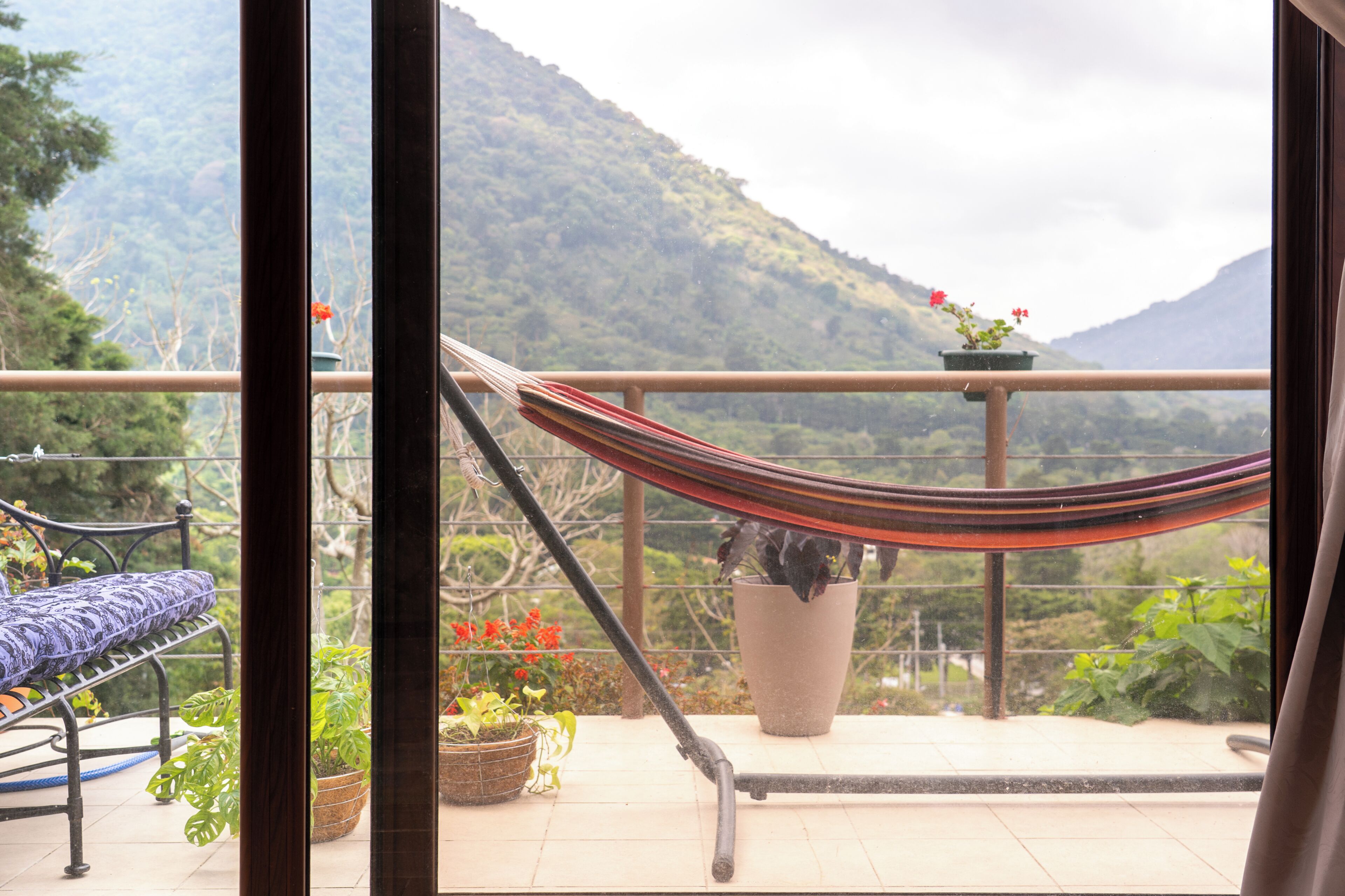 A balcony with a hammock, potted plants, and a view of a mountainous landscape.