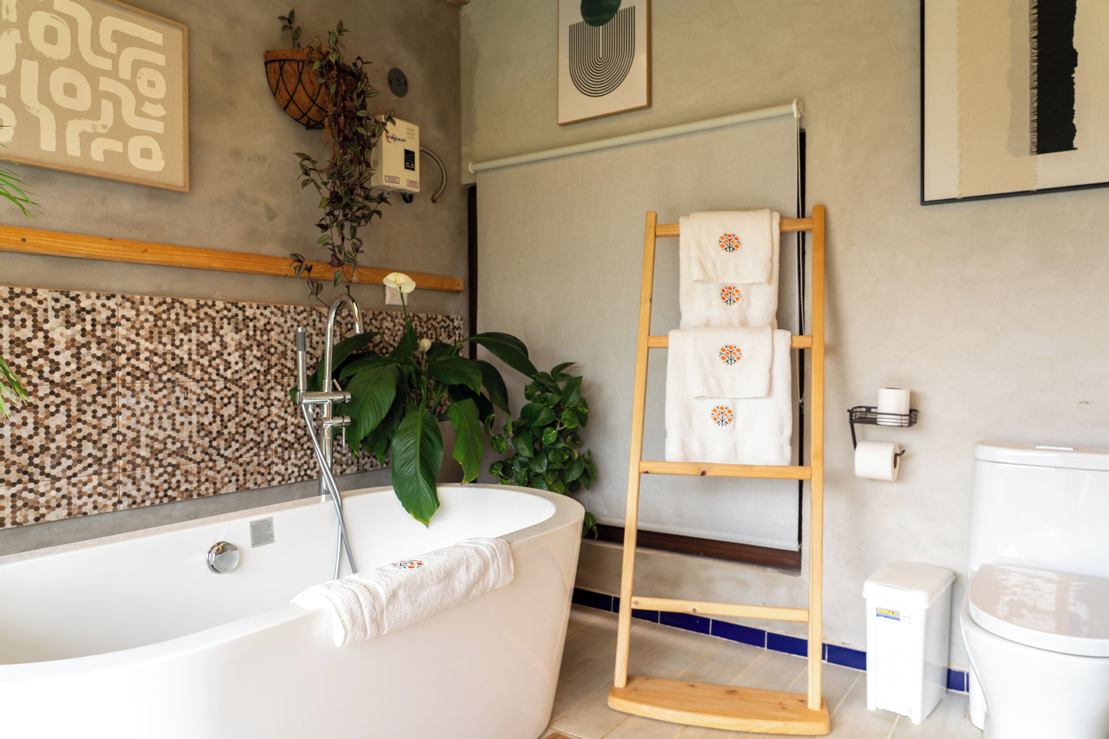 A bathroom with a freestanding bathtub, a wooden towel rack, a toilet, and a tiled wall.