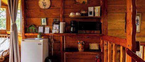 A wooden cabin interior with a refrigerator, microwave, and a clock on the wall.