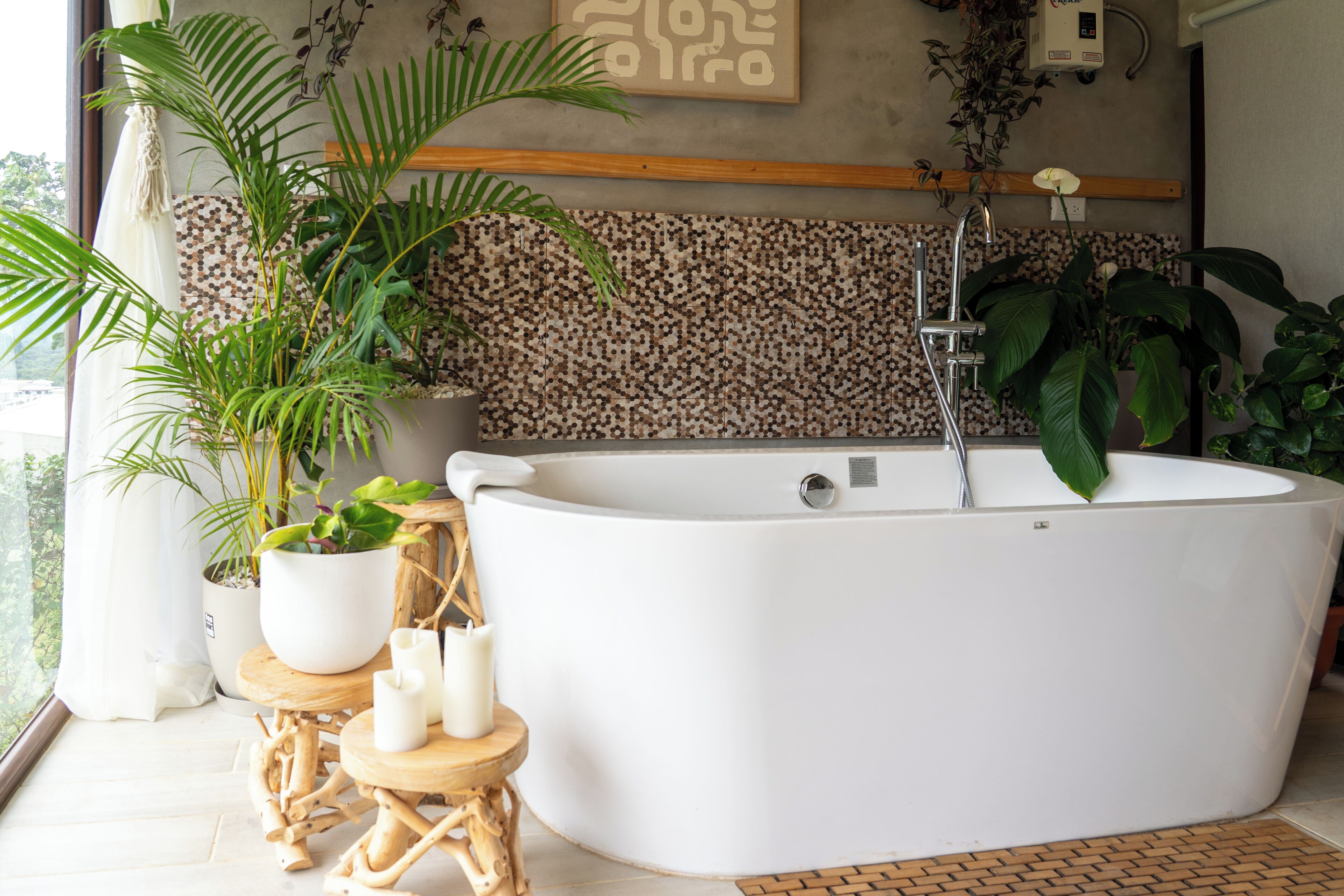A modern bathroom with a freestanding bathtub, potted plants, and a wooden stool.
