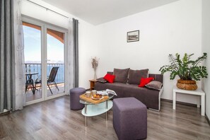 A modern living room with a sofa, a glass coffee table, a side table, and a balcony with a view.