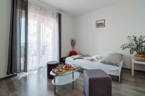 Um quarto com uma cama, uma mesa de vidro com um tabuleiro de objetos, uma planta em vaso e uma janela com cortinas.