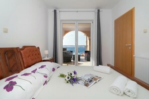 A hotel room with a bed, a view of the sea through a glass door, a wooden wardrobe, and a small table with a magazine and towels. - Comfy Apartment With Panoramic Sea View, Senj, Croatia (Senj)
