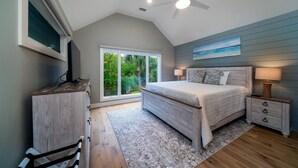 Un dormitorio con cama, mesitas de noche, ventilador de techo, ventana con persianas y vista a follaje exterior.