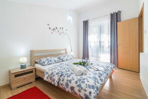 Un dormitorio con una cama de madera, una mesita de noche, un tapete rojo, un adorno de pared y una ventana con cortinas.