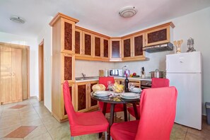 A compact kitchen with wooden cabinets, a white refrigerator, and a dining table with red chairs. - Comfy Sunset And Sea View Apt /w Jacuzzi, Senj, Croatia (Senj)