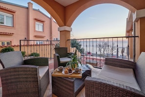 A balcony with wicker furniture, a tray with food and drinks, and a view of the cityscape.
