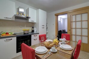 Cozinha moderna com armários brancos, uma mesa de jantar posta com pratos, copos e uma cesta de pão.