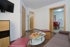 Un soggiorno moderno con un tavolino in vetro, sedute imbottite rosse, un televisore a schermo piatto e un'area pranzo sullo sfondo.