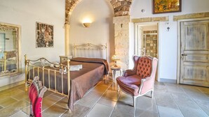 Un dormitorio con un arco de piedra, una cama con cabecera, una silla, una lámpara y una puerta.