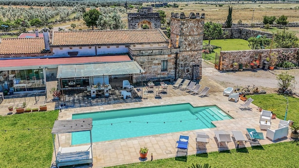 Un área de piscina con sillones de descanso, un edificio de piedra y vistas del paisaje circundante.