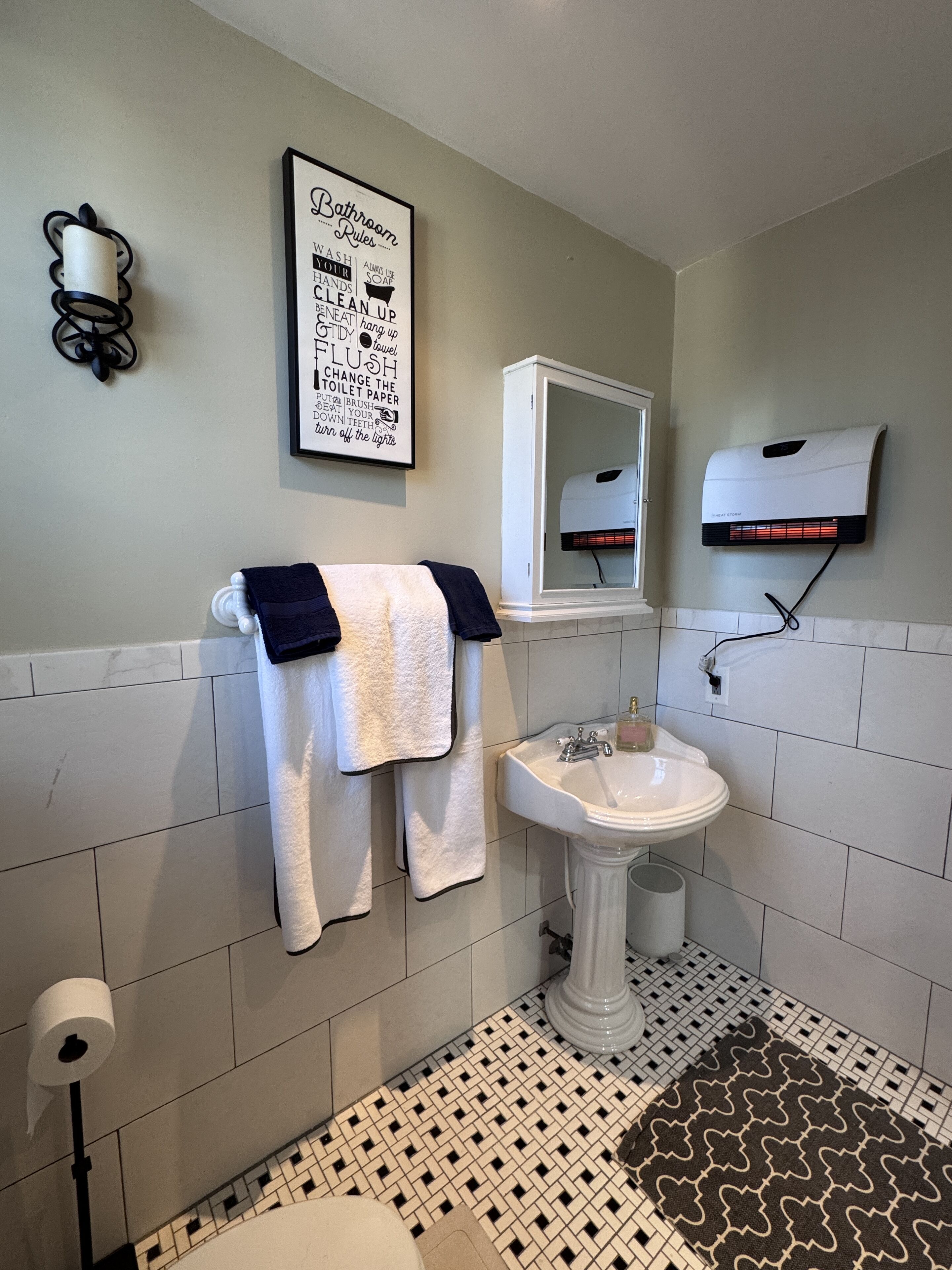 A bathroom with a sink, towel rack, and a framed sign with bathroom rules.